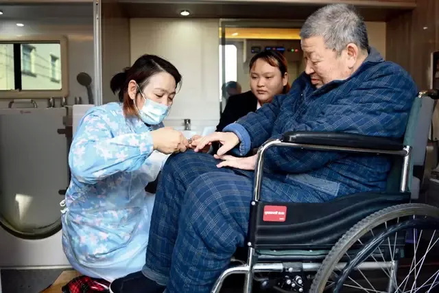 助浴师在移动助浴车为一名81岁的老人（右一）修剪指甲