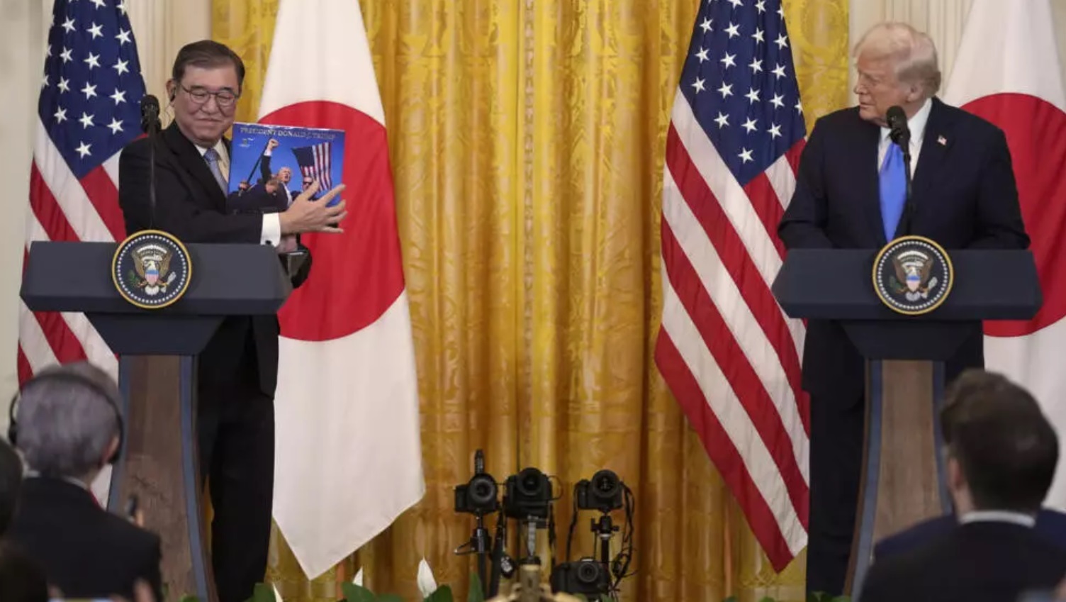 Japan's Prime Minister Shigeru Ishiba holds up a book presented by President Donald Trump during a n ...