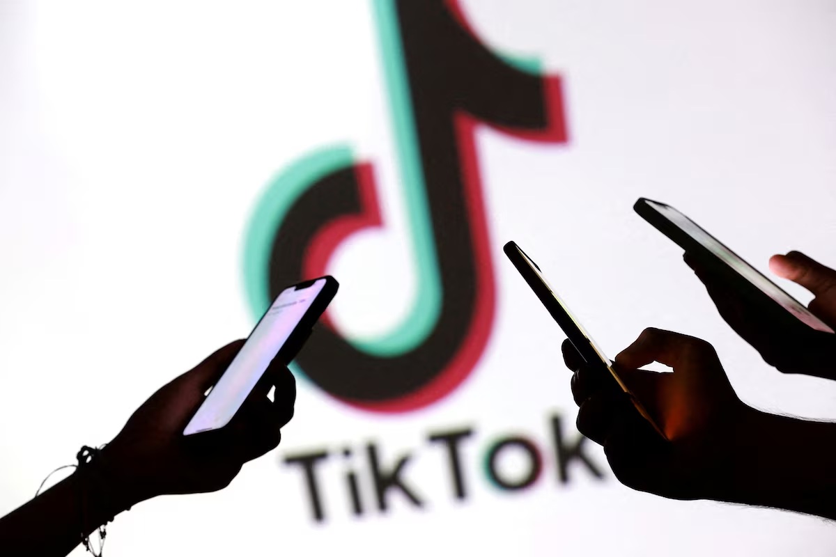 照片中的青少年手持智能手机，在 TikTok 标志前摆姿势拍照